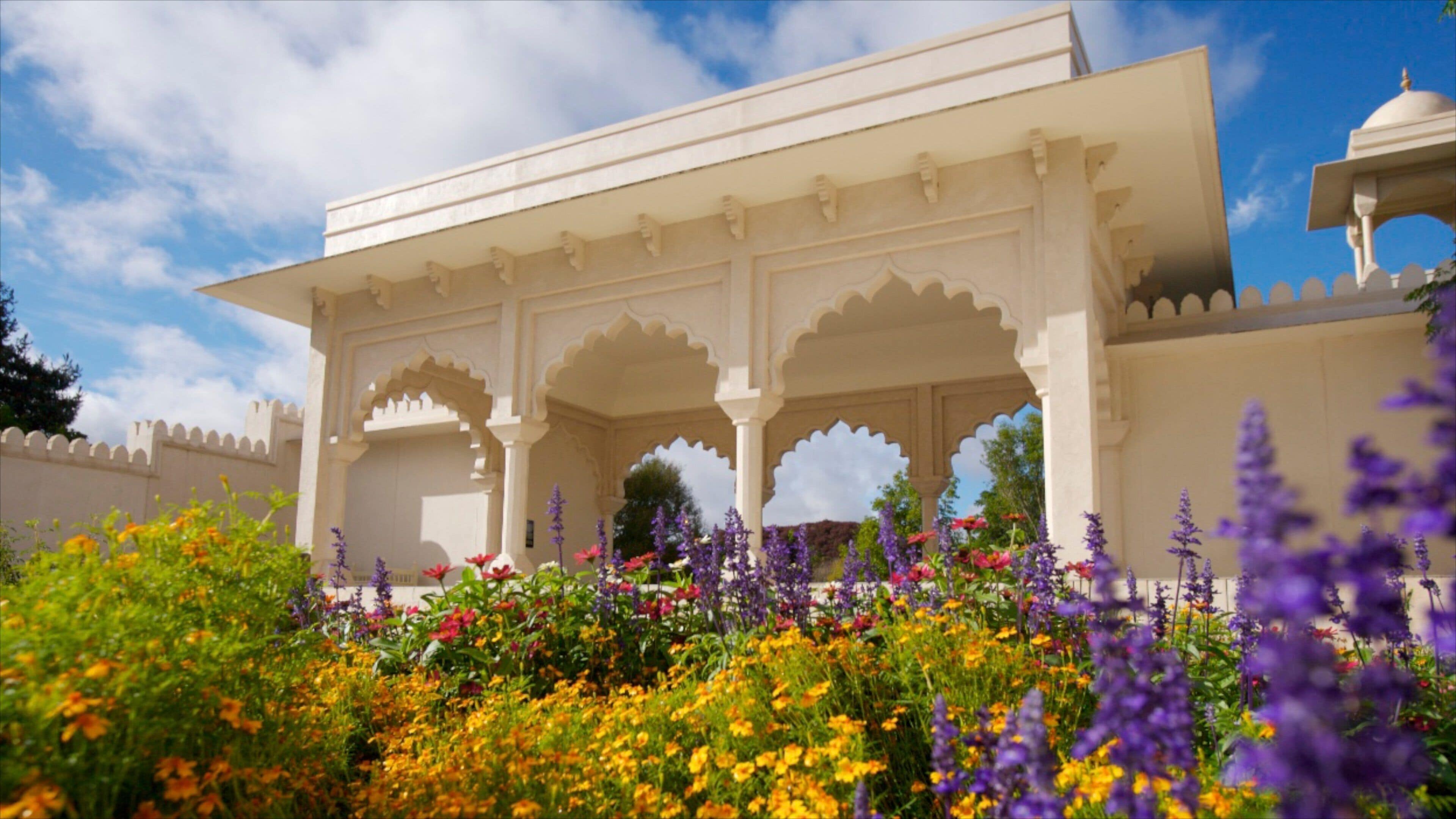 A white pavilion with arches, surrounded by colorful flowers and purple plants.