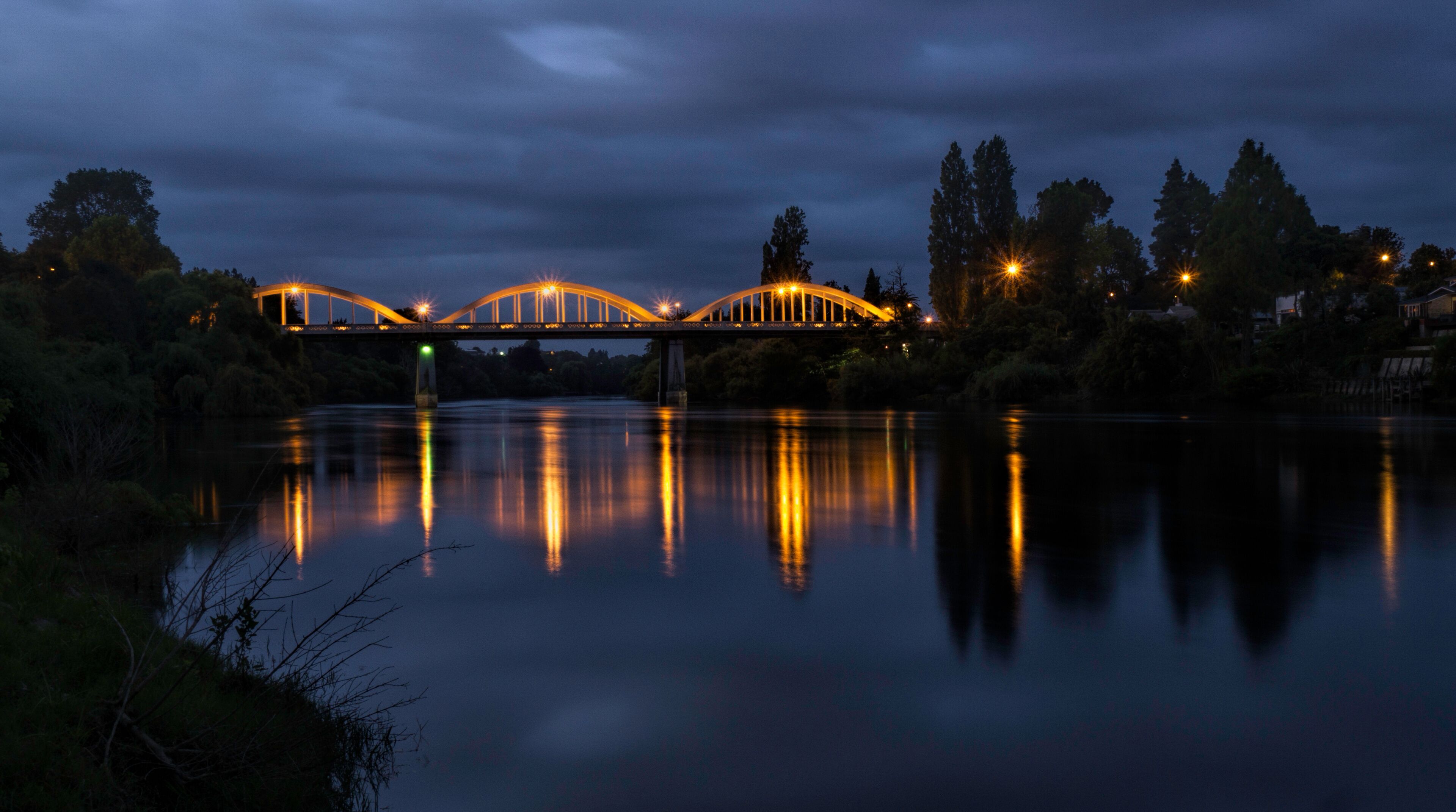 A bridge with lights reflecting on a calm river at night.