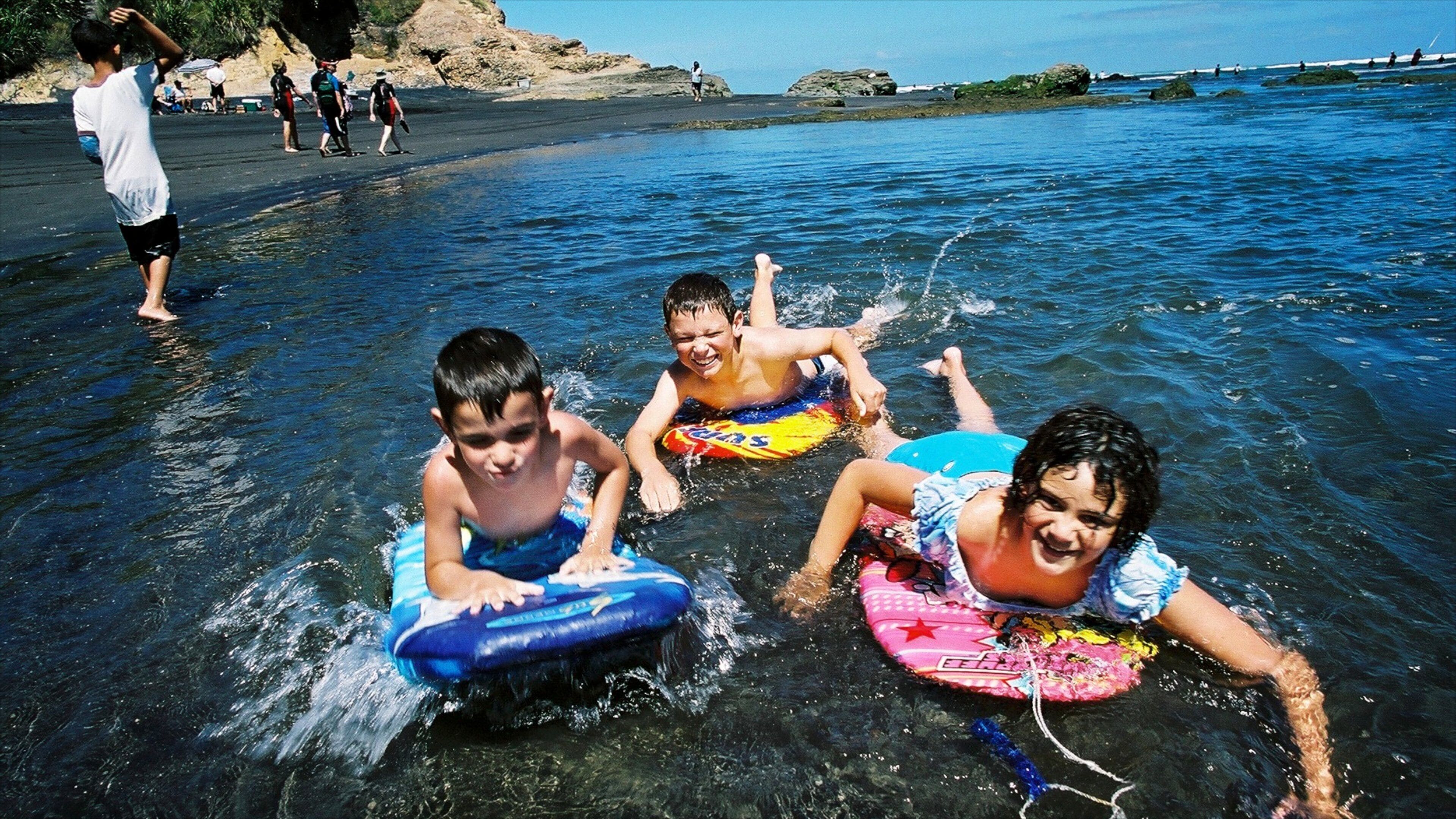 Children on waterboards at a beach with rocky formations in the background.