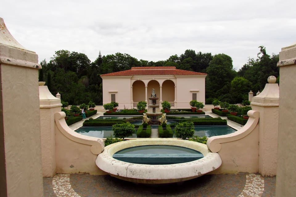 Un edificio clásico con una fuente y una piscina en un jardín formal.