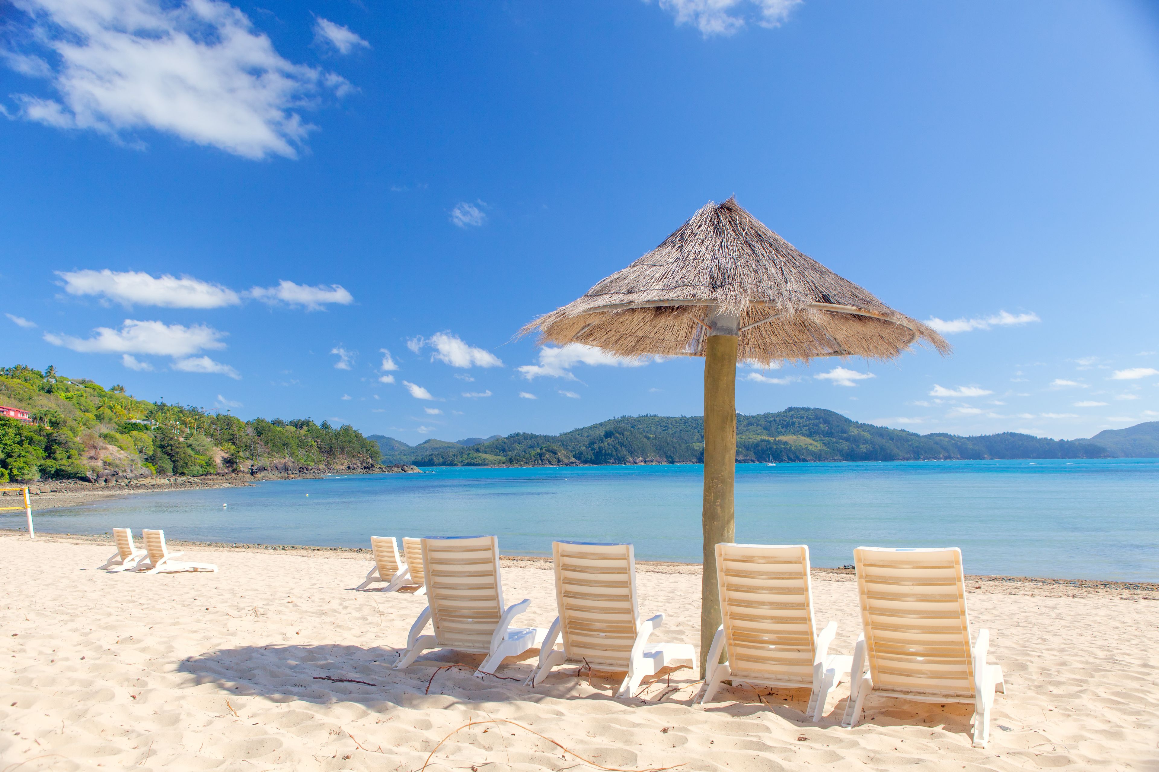 A beach with white lounge chairs and a thatched umbrella.