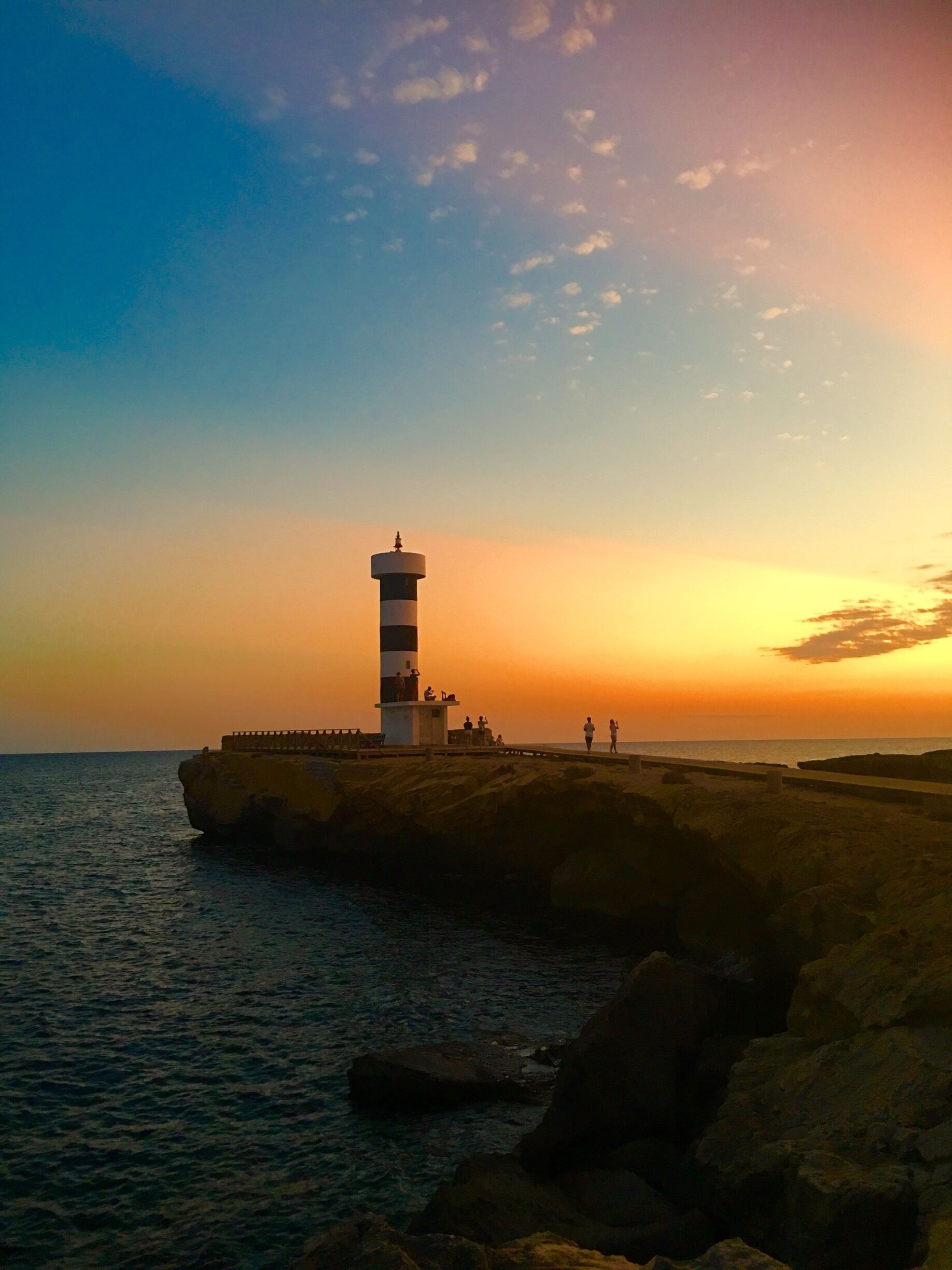 A lighthouse on a rocky outcrop by the sea at sunset.