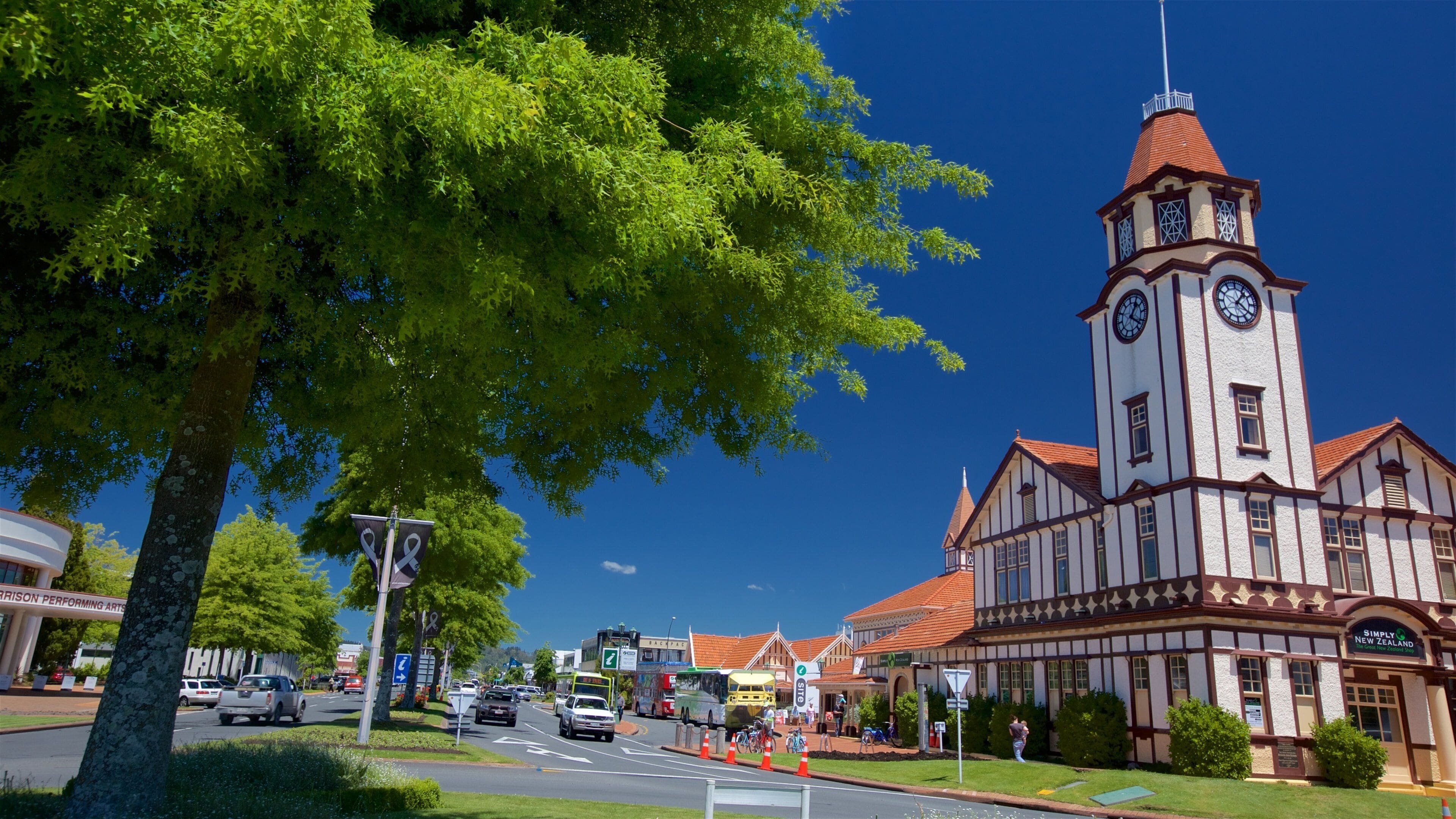 A town square with a clock tower, a bus, and a building with a sign that reads "Simply New Zealand."