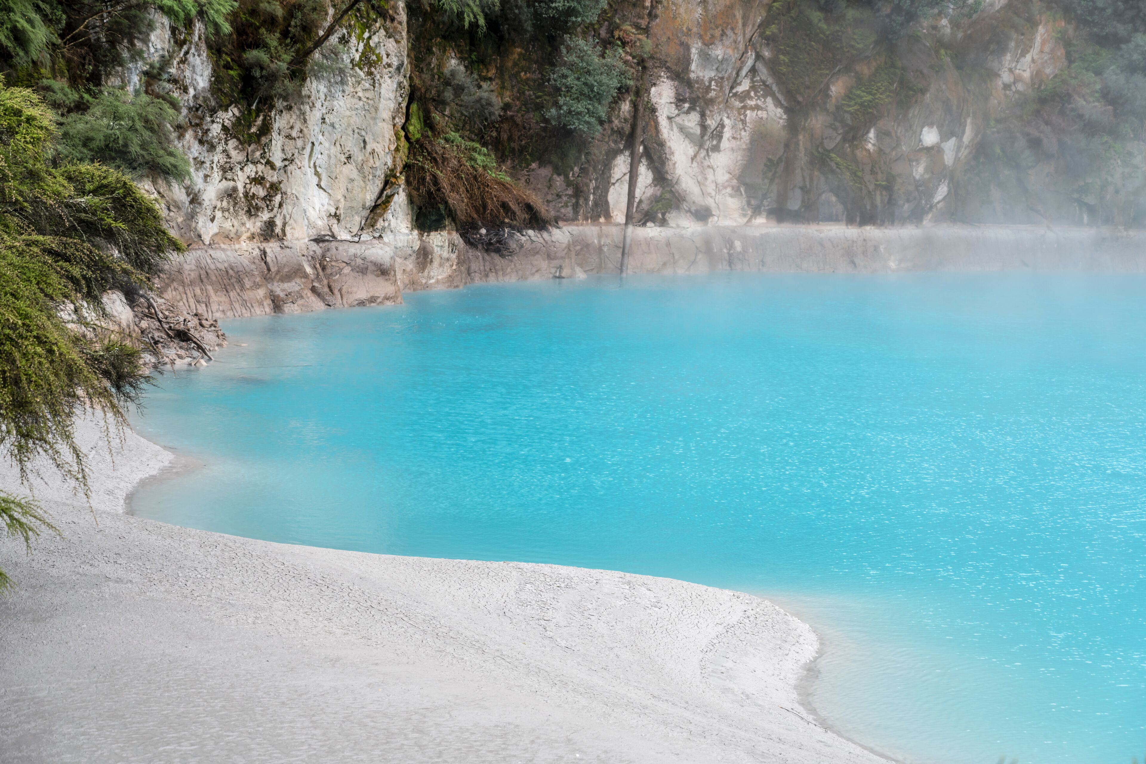 Uma piscina azul-turquesa rodeada por areia branca e falésias rochosas.