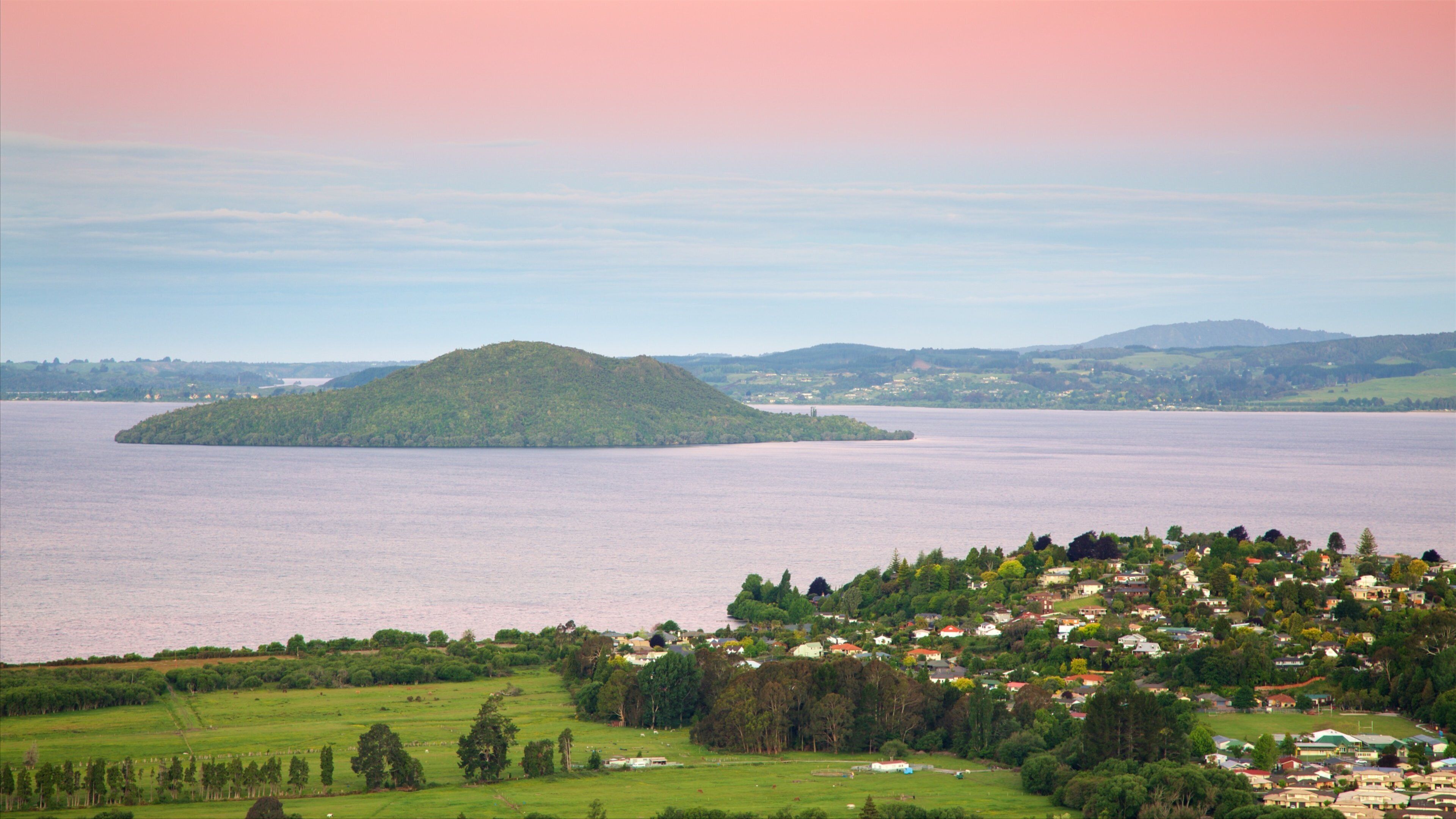A coastal town with a large body of water, a small island, and rolling hills in the background.