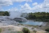 A geothermal area with a hot spring, steam rising, and a turquoise pool surrounded by rocky terrain and greenery.