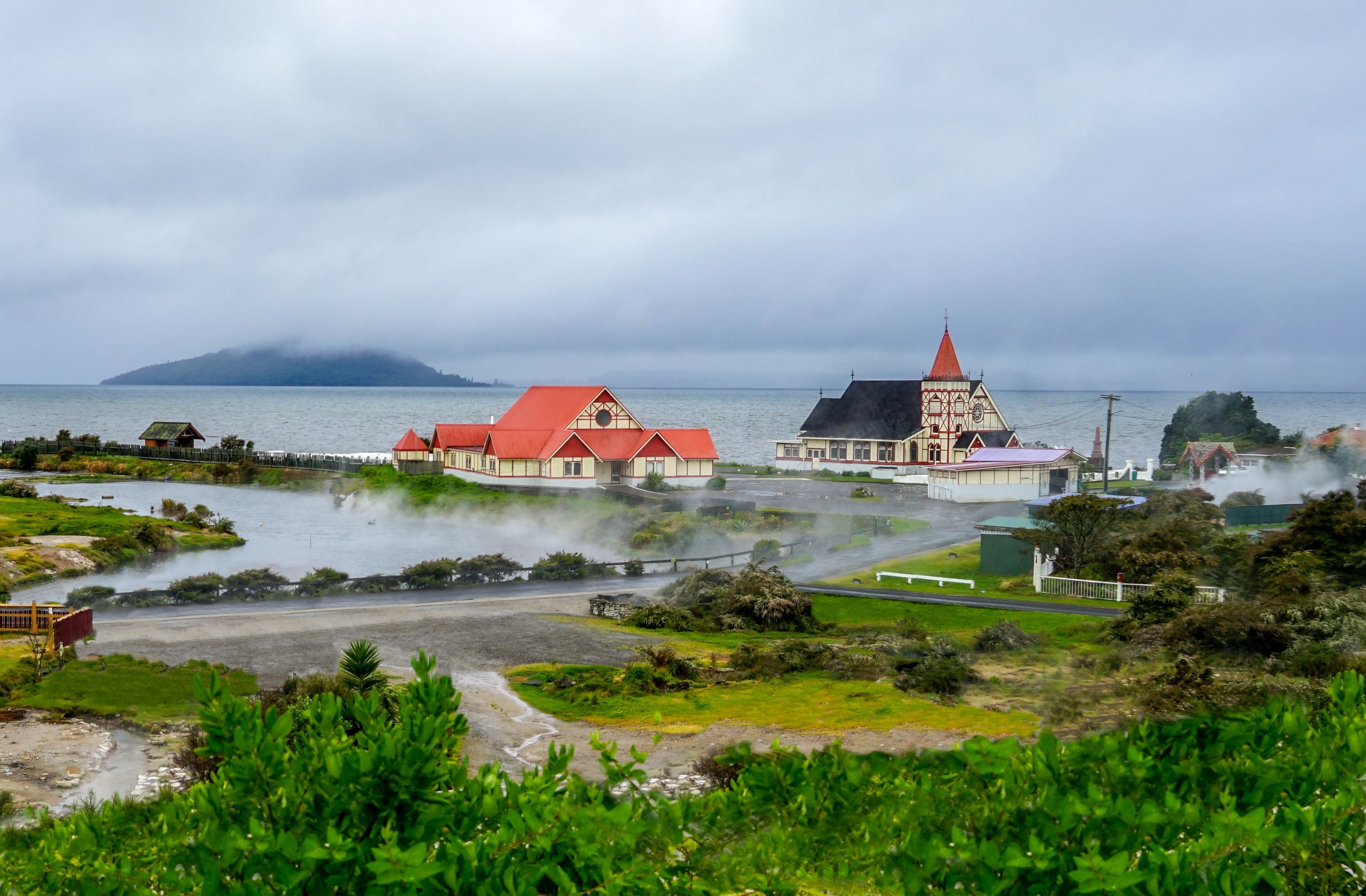 Une ville côtière aux bâtiments aux toits rouges, une église surmontée d’un clocher rouge et une baie enveloppée de brume.
