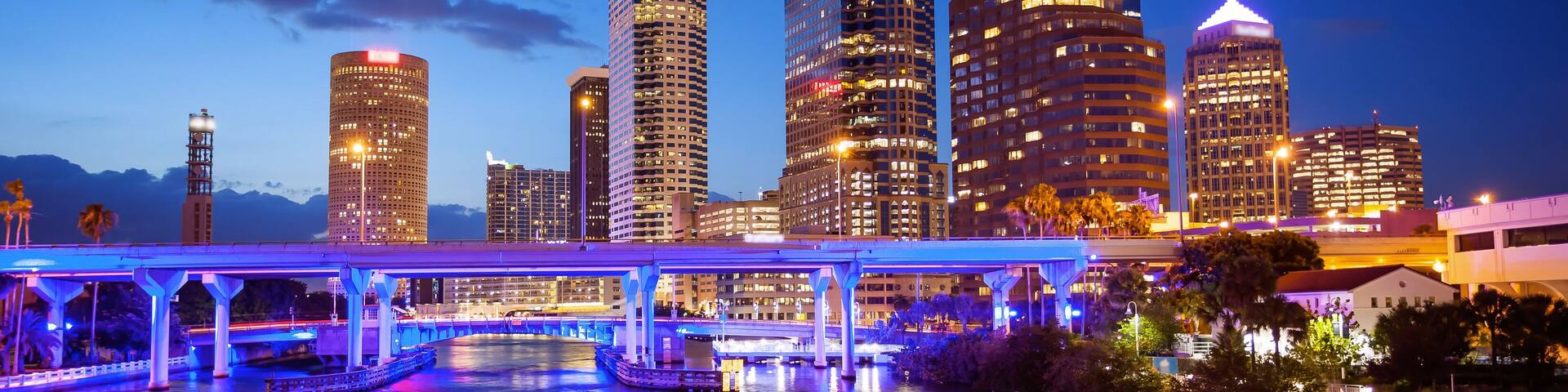 A city skyline with illuminated buildings and a bridge over a reflective water body.