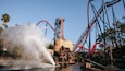 Une fontaine, des montagnes russes et des palmiers dans un parc d’attractions.