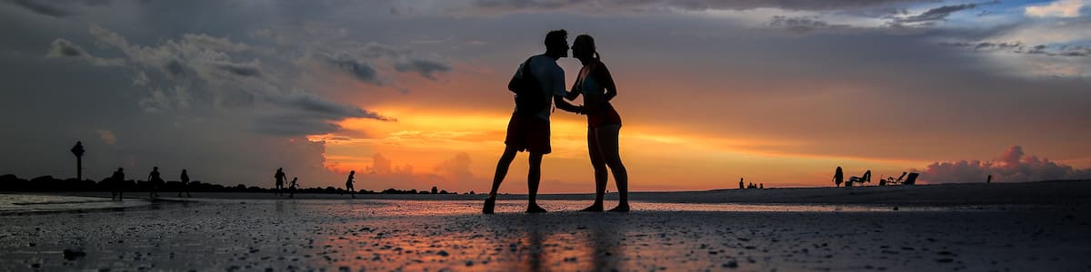 A couple embracing on a beach at sunset with silhouettes against the sky.