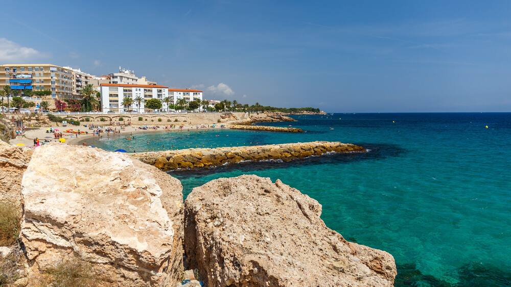 A coastal town with clear turquoise waters, rocky outcrops, and a sandy beach.
