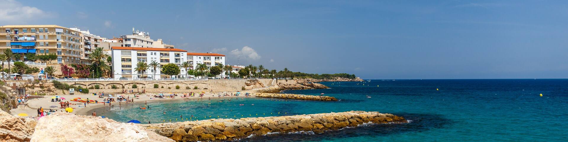 A coastal town with clear turquoise waters, rocky outcrops, and a sandy beach.