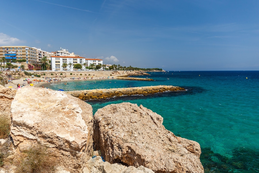Un pueblo costero con aguas turquesas cristalinas, afloramientos rocosos y una playa de arena.
