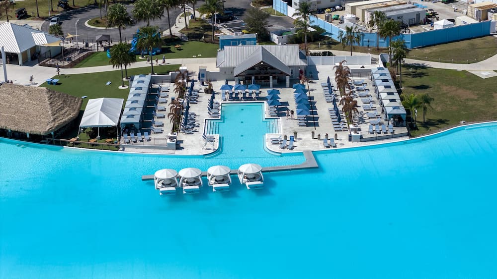 Wesley Chapel, United States - 02 March 2026: Aerial view of Epperson Lagoon featuring turquoise water, floating white cabanas, blue umbrellas on the sun deck, and palm trees.