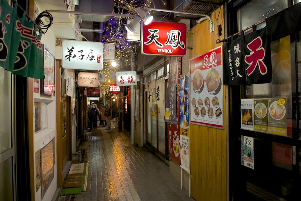 A narrow alley with shops, signs in Chinese, and wet pavement.