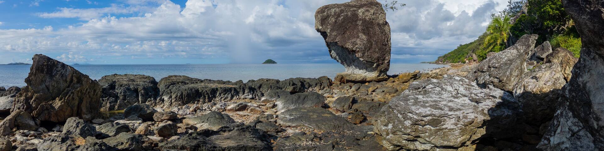 Large rock on rocky shoreline of a Fiji island panorama