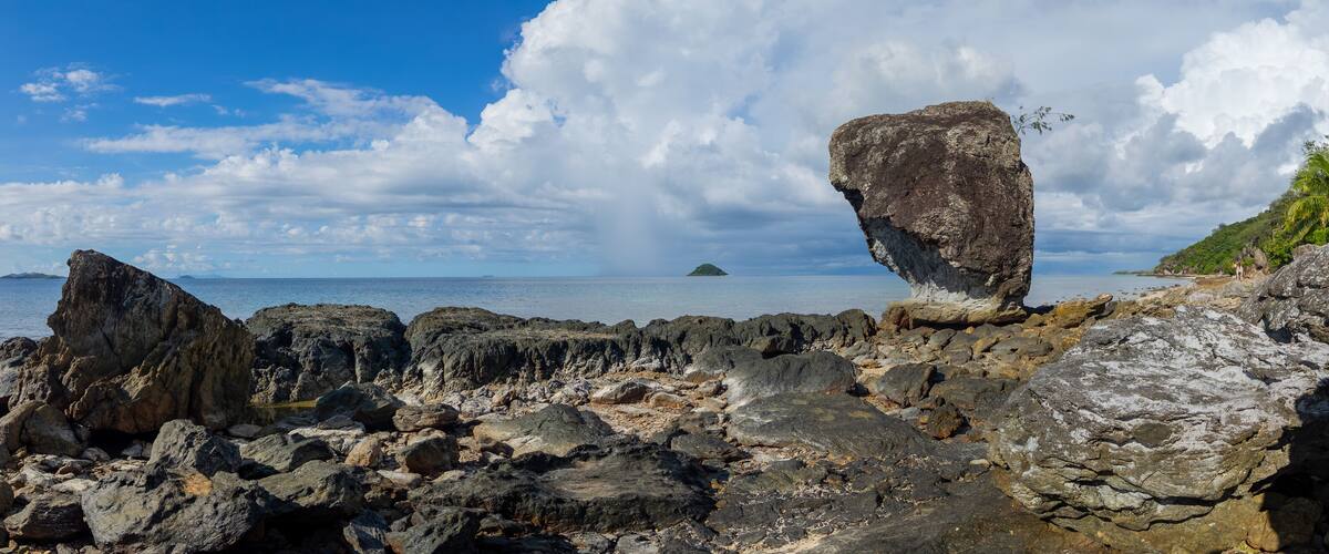 A rocky coastline with a prominent rock formation and a distant island.