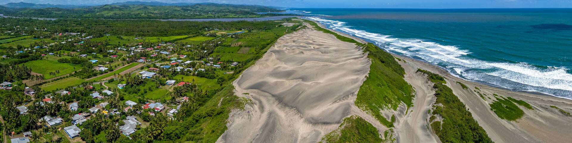 A coastal landscape with a sandy beach, a small village, and rolling hills in the background.