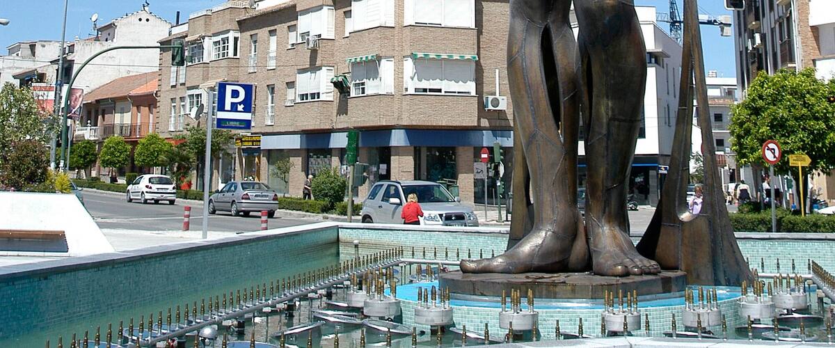 A large bronze statue of a woman in a dynamic pose, set against a clear blue sky and urban backdrop.