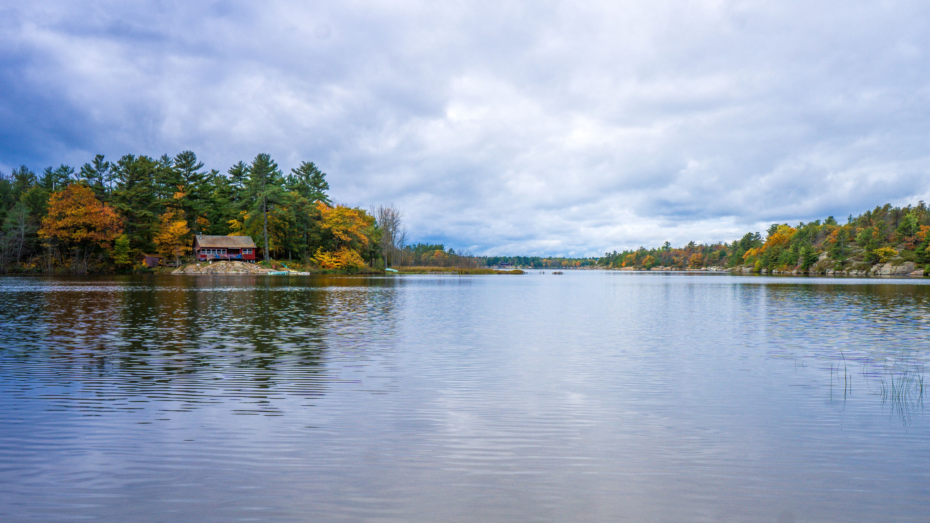 A calm lake with a red cabin on the left and autumn-colored trees on both sides.