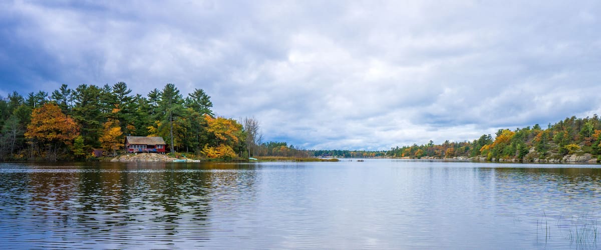 A calm lake with a red cabin on the left and autumn-colored trees on both sides.