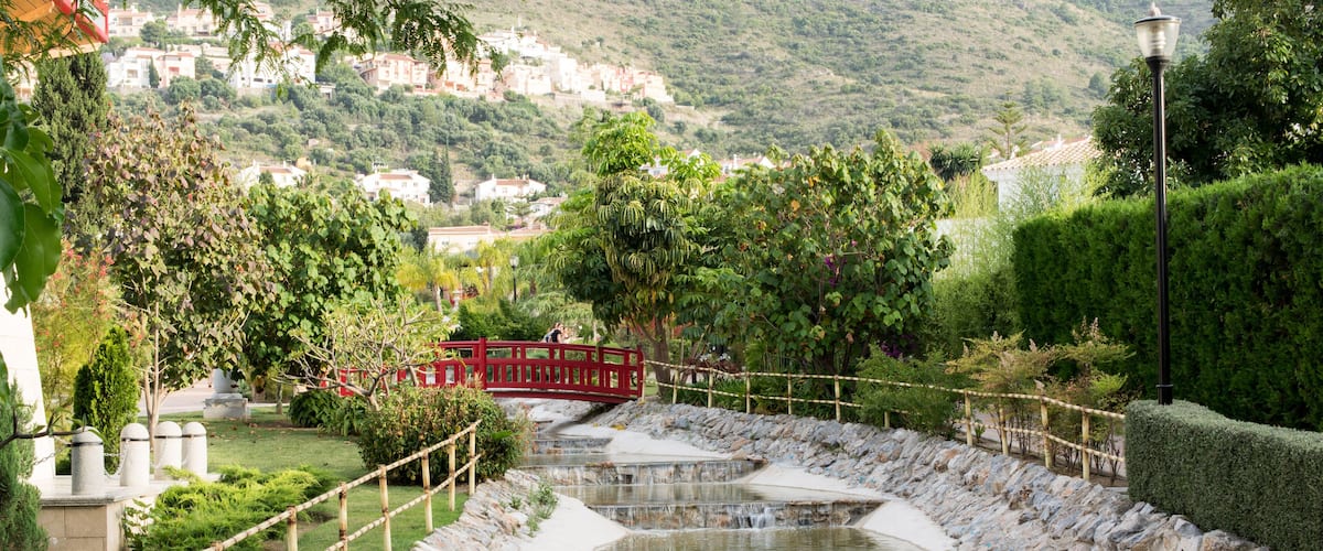 A terraced water feature with a red bridge, surrounded by greenery and a hillside in the background.