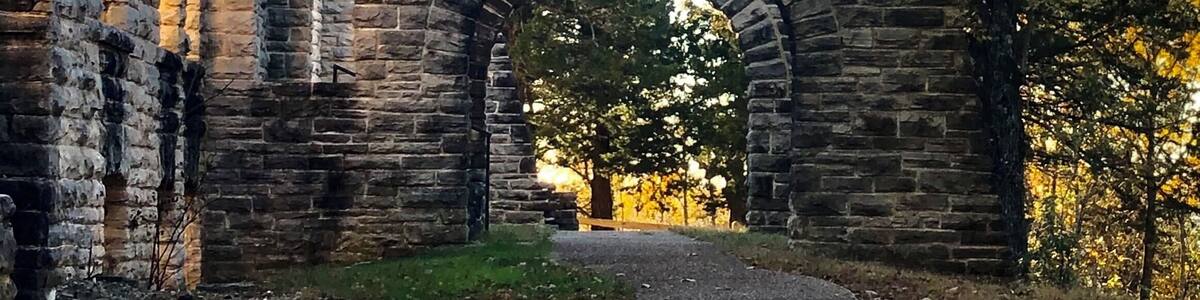 An old stone archway leading through a wooded area.