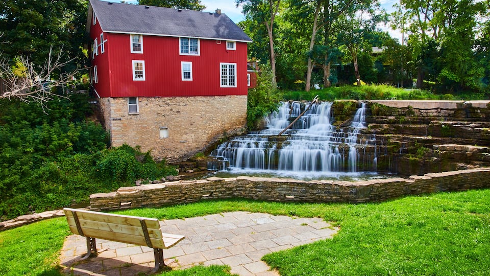 A red house, a stone bench, and a waterfall.