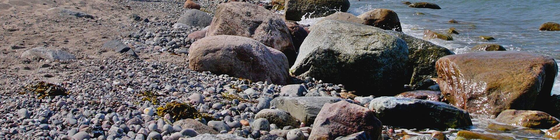A rocky beach with large boulders and a cliff in the background.