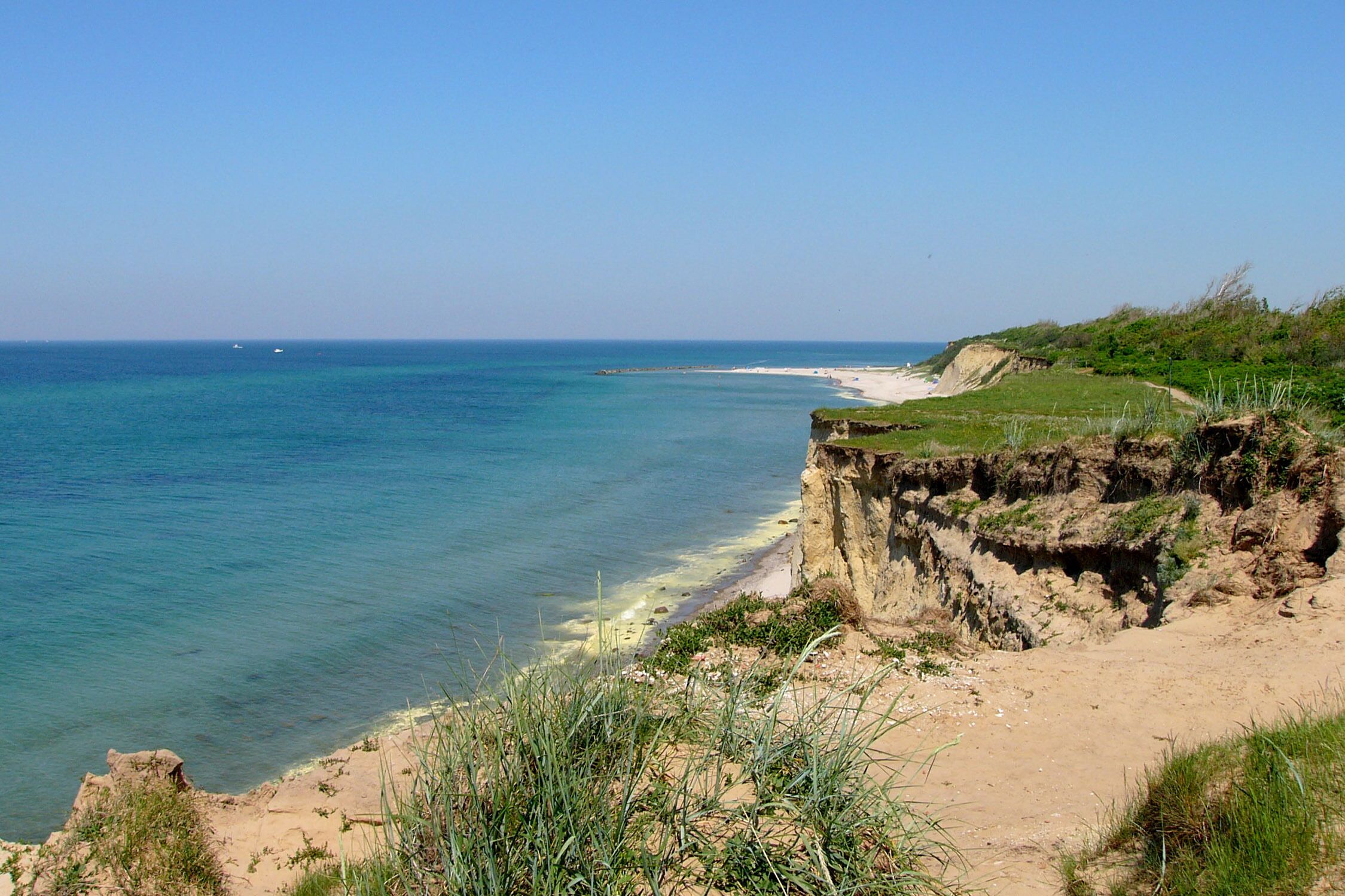 A coastal landscape with a sandy beach, a cliff, and the ocean.