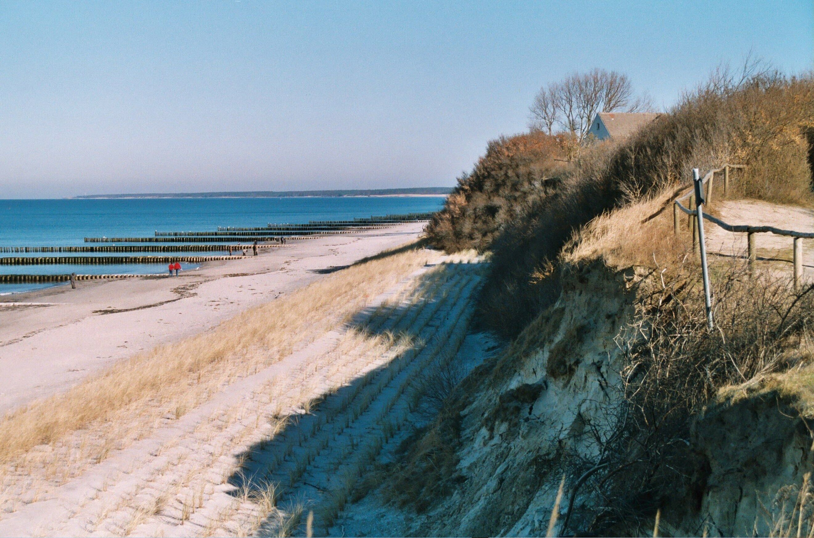 A sandy beach with a wooden walkway, a pier, and a distant building.