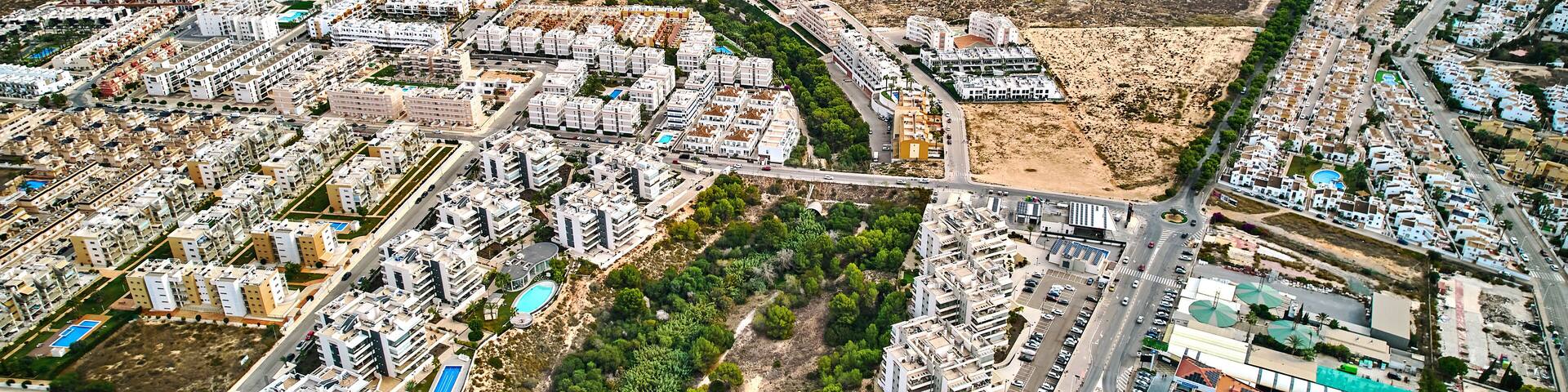 An aerial view of a coastal city with dense residential areas, a large open field, and a marina.