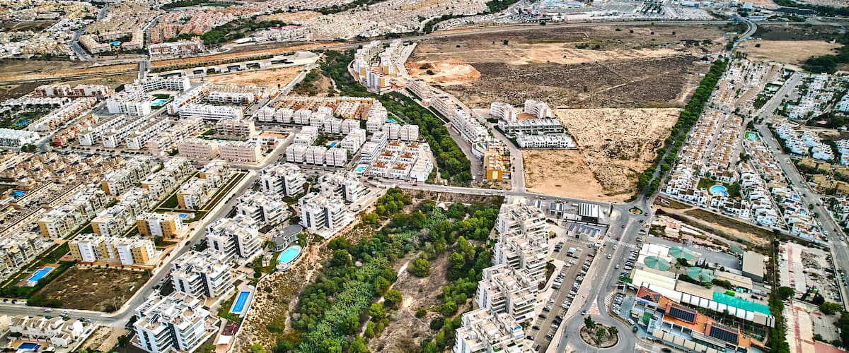 An aerial view of a coastal city with dense residential areas, a large open field, and a marina.