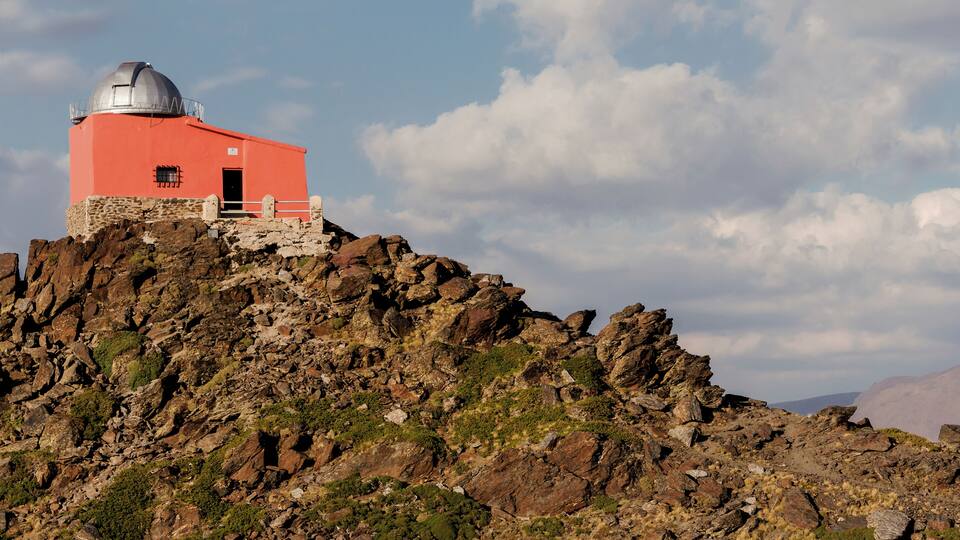 A red observatory on a rocky hill with a clear sky.