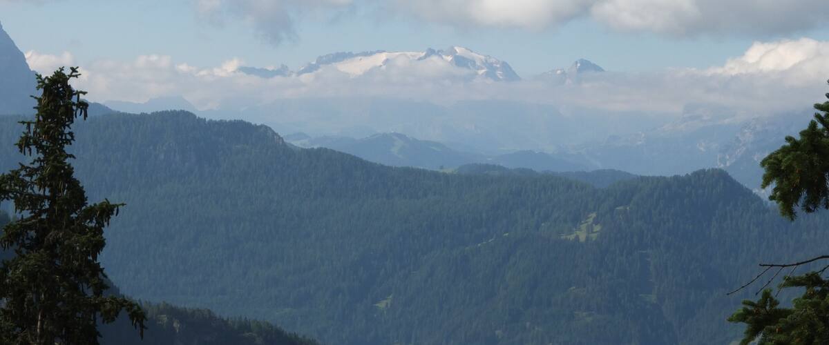 A mountain range with snow-capped peaks and a forested valley.