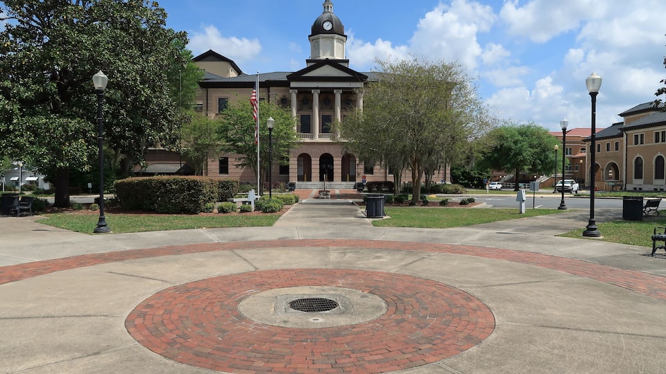 A historic building with a clock tower, surrounded by a landscaped courtyard with a circular brick pattern and trees.