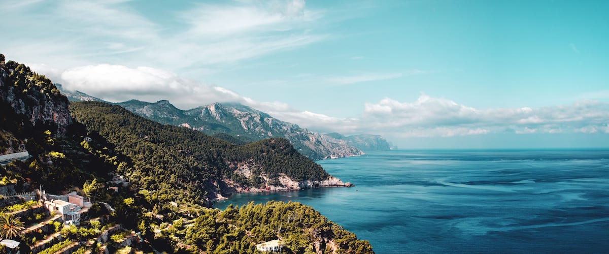 Un paisaje costero con montañas, cielo despejado y mar tranquilo.