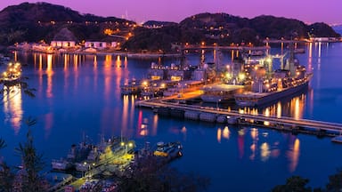Un port au crépuscule, avec des bateaux illuminés et un grand navire amarré.