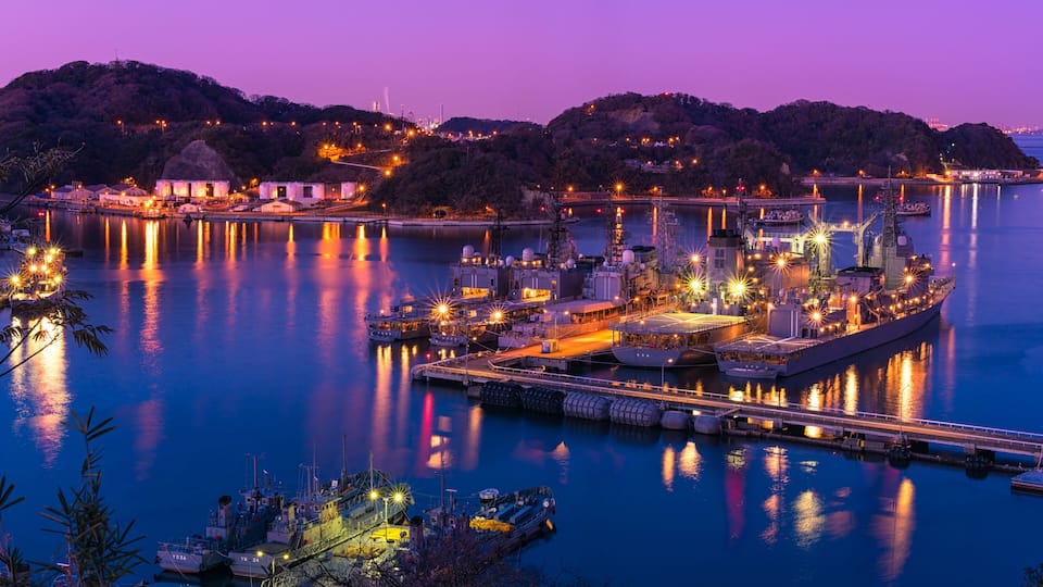 A harbor at dusk with illuminated boats and a large ship docked.