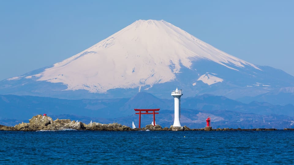 A lighthouse, a red torii gate, and a snow-capped mountain in the background.