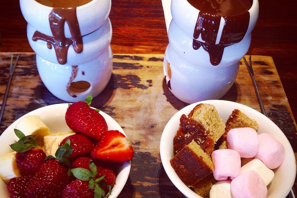 Two cups of hot chocolate with chocolate sauce, a bowl of strawberries, and a bowl of marshmallows.