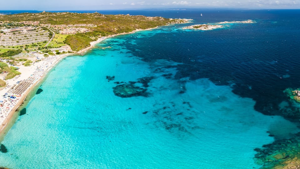 A coastal resort with a turquoise beach, clear waters, and a hilly landscape.
