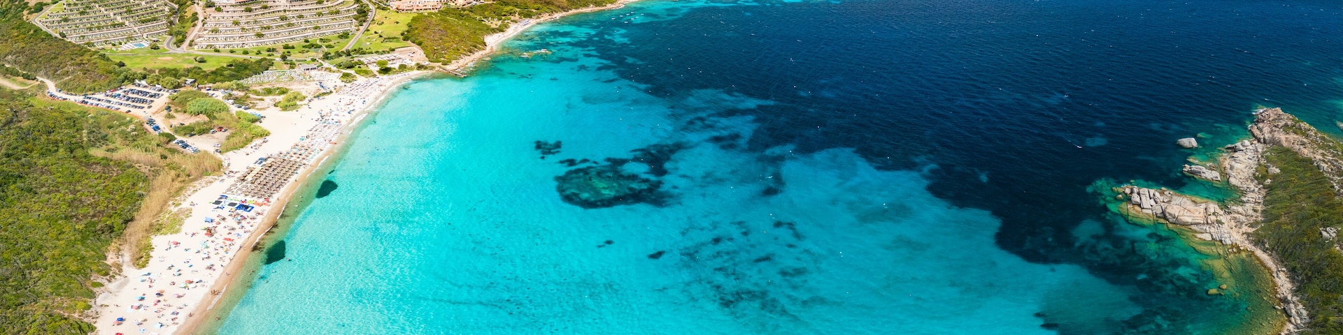 A coastal resort with a turquoise beach, clear waters, and a hilly landscape.