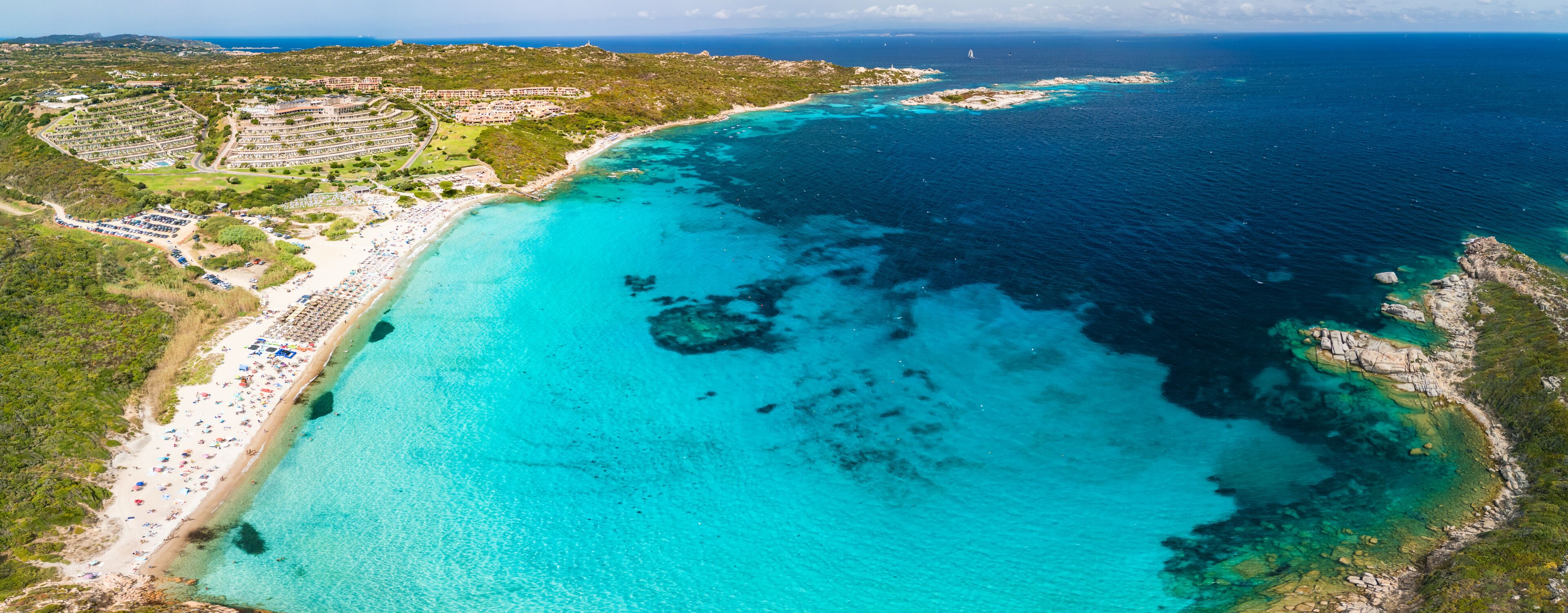 A coastal resort with a turquoise beach, clear waters, and a hilly landscape.