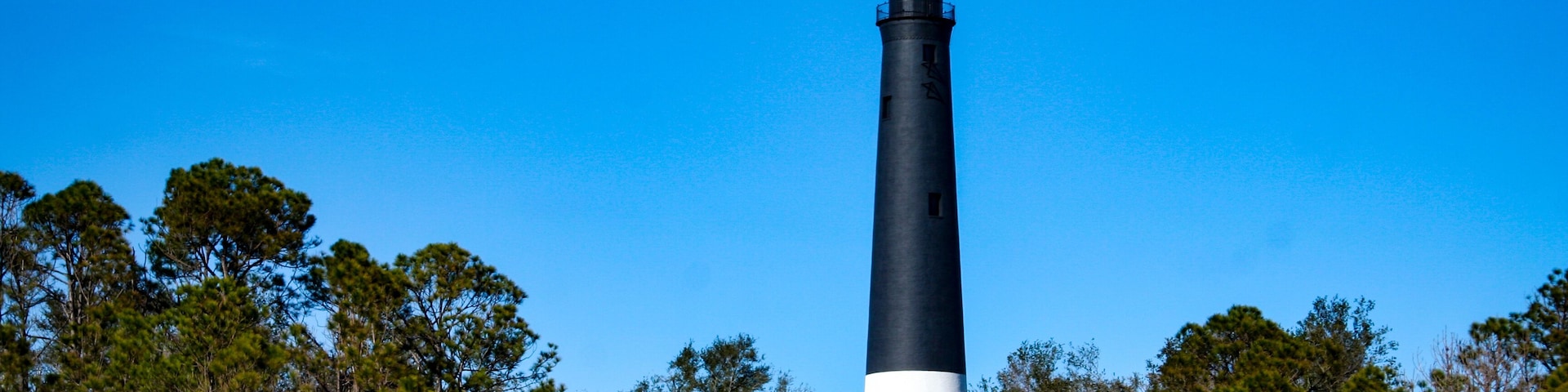 Um farol alto, em preto e branco, rodeado por árvores.