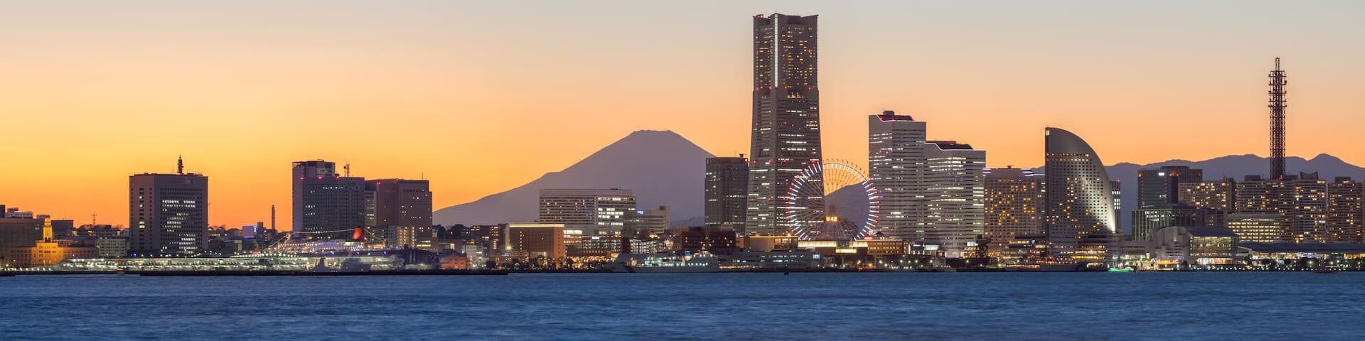 A city skyline with a prominent skyscraper, a large Ferris wheel, and a mountain in the background.