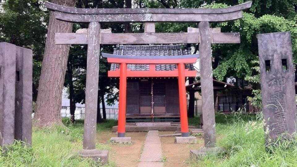 A traditional Japanese torii gate with a red upper section and a grey lower section, surrounded by trees and a stone pathway.