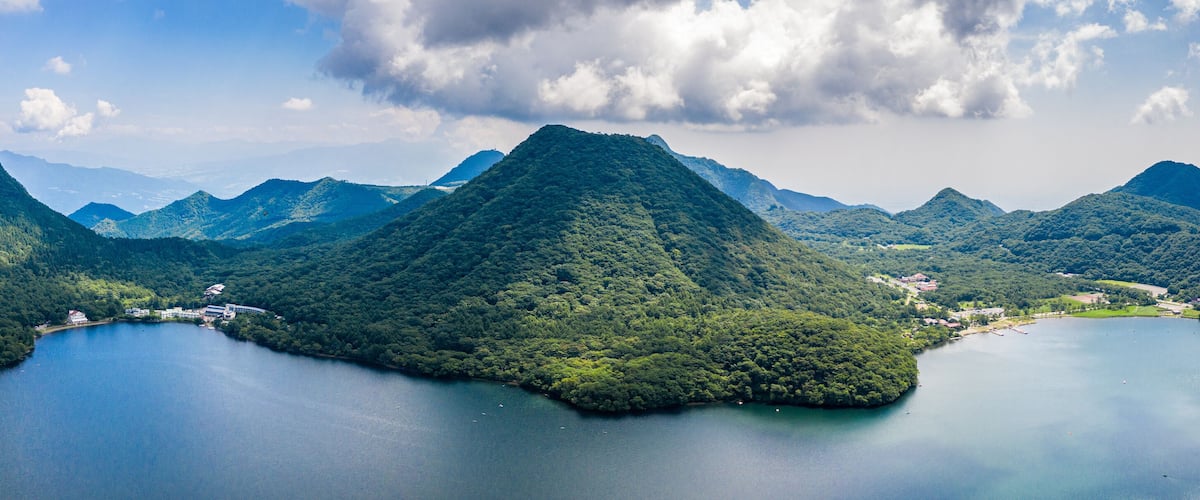 A mountainous landscape with a lake surrounded by dense forests and a few buildings.