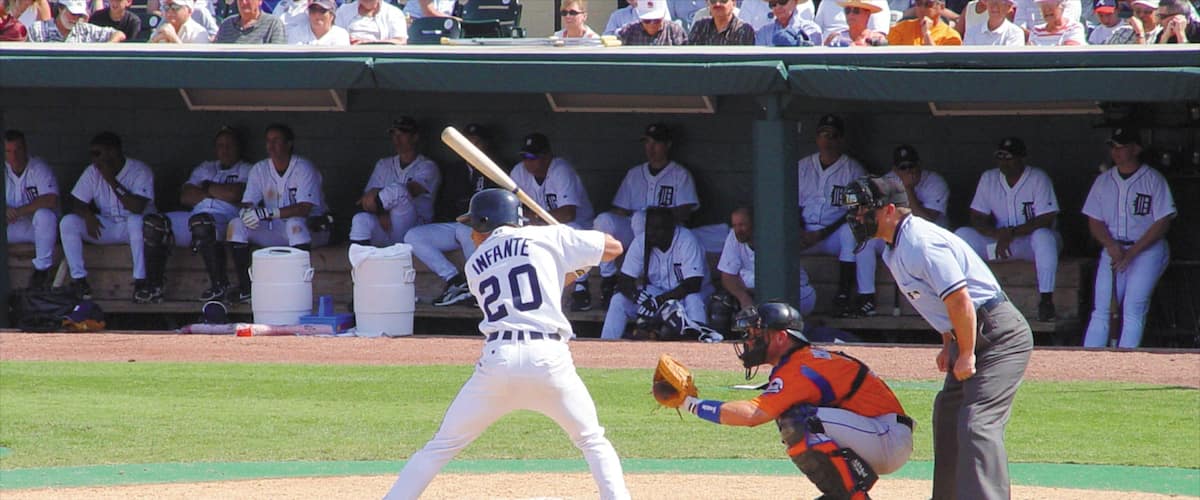 A baseball player in a white uniform with the number 20, a catcher in an orange uniform, and an umpire standing behind the catcher.