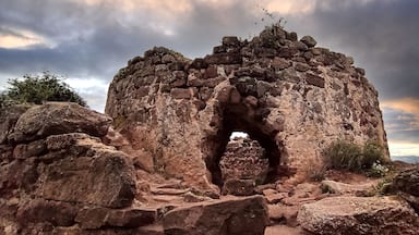 Una gran formación rocosa con un arco central, rodeada de rocas más pequeñas y vegetación escasa.